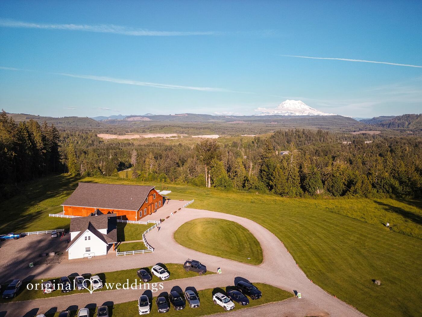 Aerial view of the cedar barn, white bridal cottage, and circular drive with Mount Rainier on the horizon
