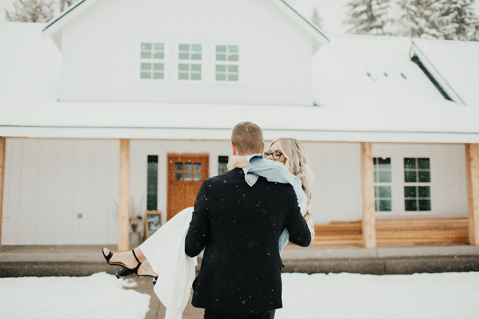 Groom carrying his bride toward the snow-covered bridal cottage