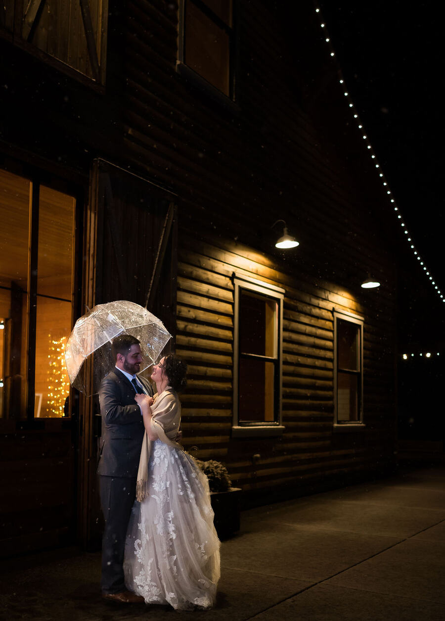 Couple under a clear umbrella outside the glowing barn at night