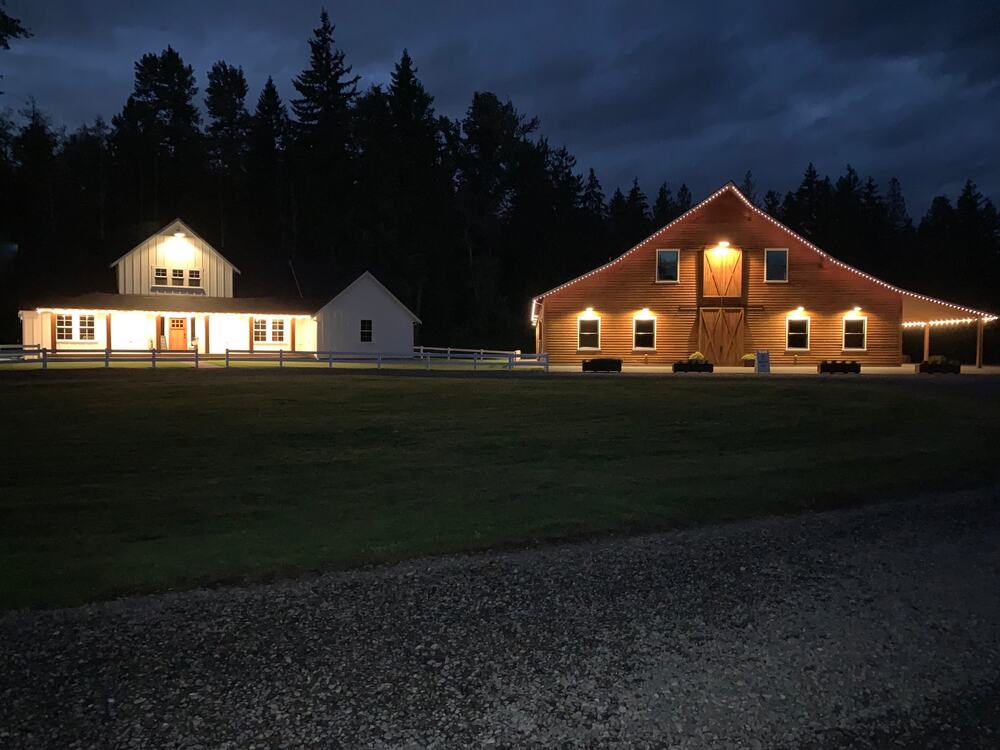 The bridal cottage and barn lit up at night beside the gravel lot