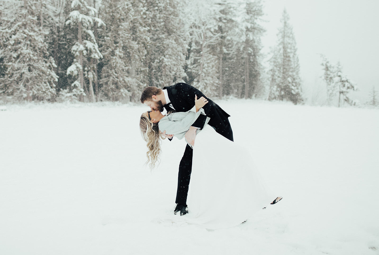 Couple kissing in the snow-covered meadow with snowy firs behind