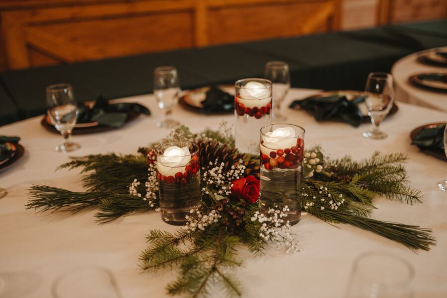 Floating candles with cranberries in glass cylinders on a bed of evergreens and baby's breath