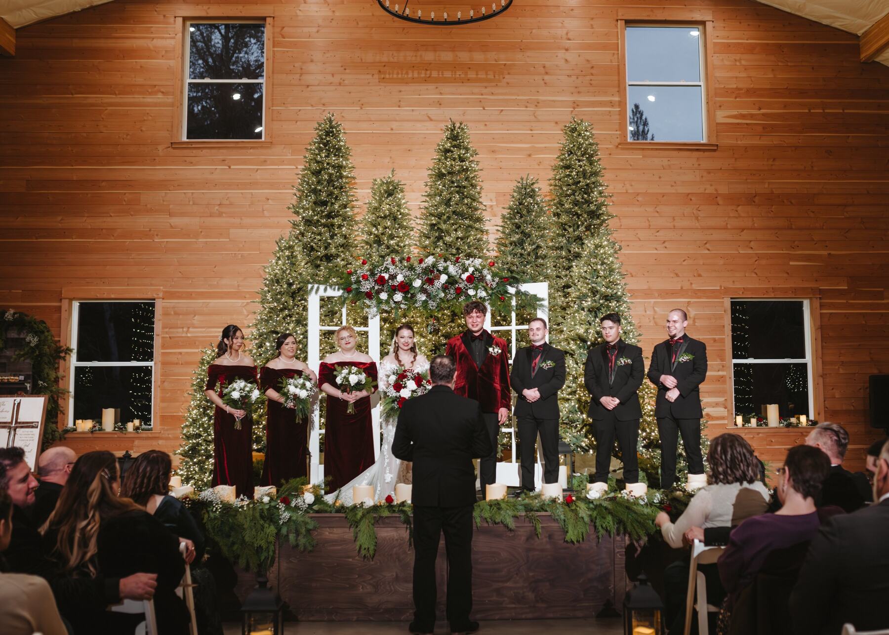 Tahlia and Baxter with their wedding party in front of a wall of lit Christmas trees during their indoor ceremony