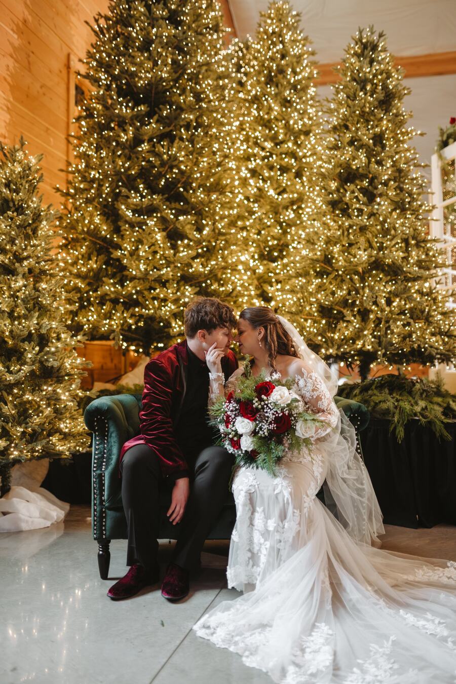Couple touching foreheads on a green velvet loveseat in front of lit Christmas trees