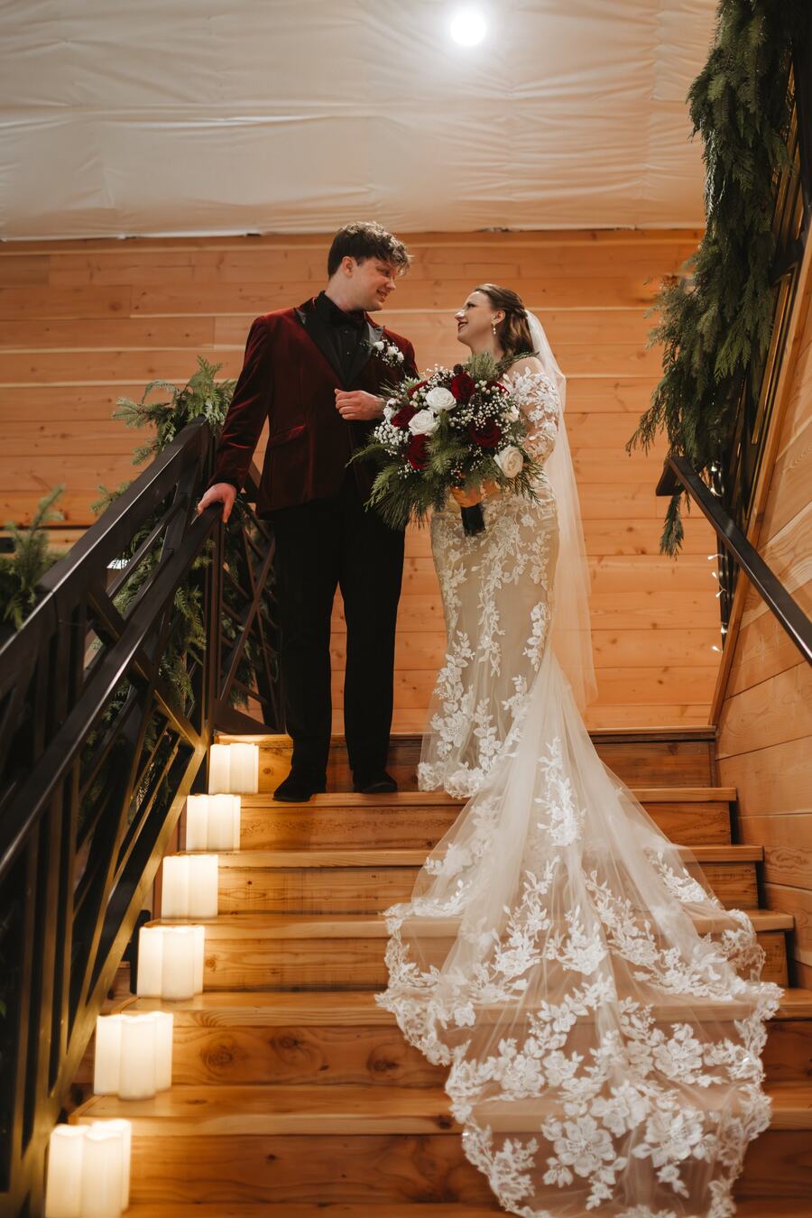 Couple smiling at each other at the top of the garland-wrapped staircase