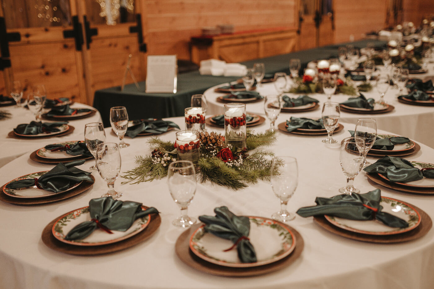Round reception tables set with gold chargers, green napkins, and evergreen centerpieces