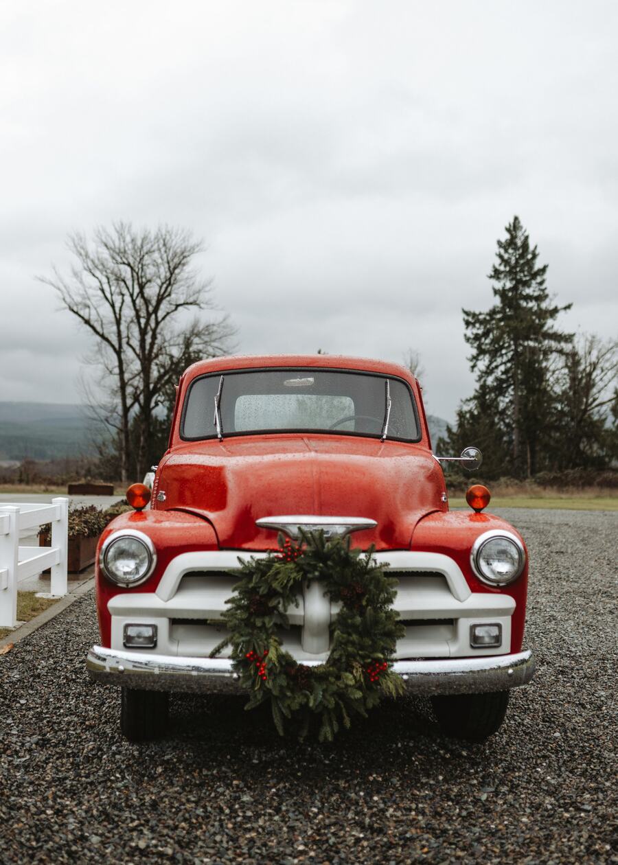 Vintage red pickup truck with a wreath on the grille parked on the gravel drive