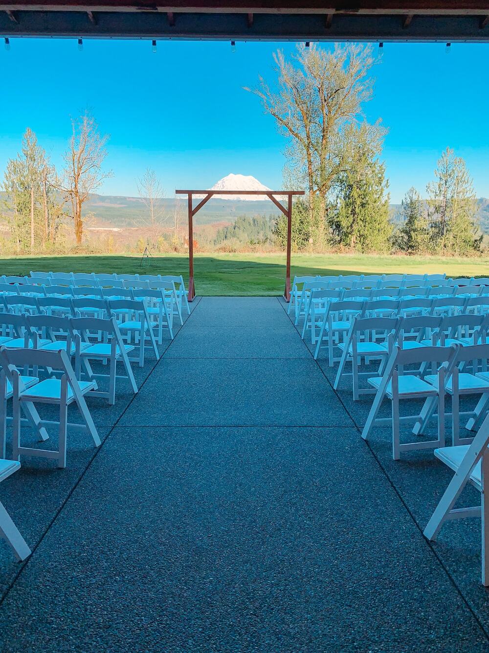 Aisle of white chairs on the patio leading to the arbor with Mount Rainier beyond