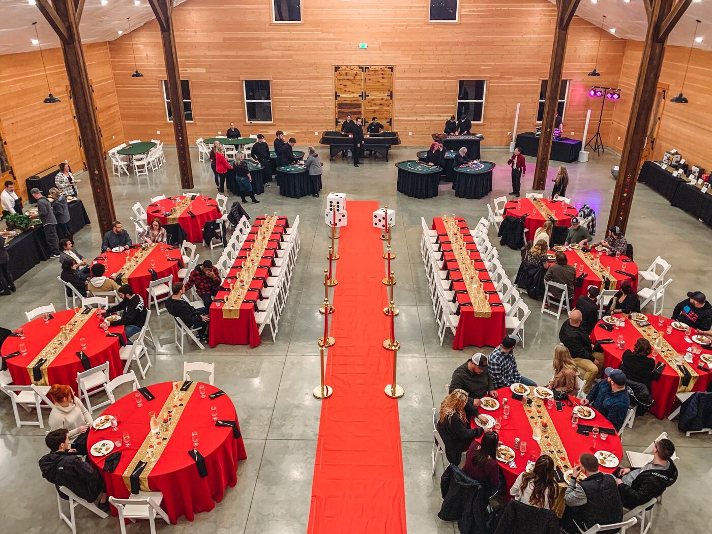 Overhead view of a casino night fundraiser in the barn, with red-draped tables, a red carpet, and blackjack and craps tables