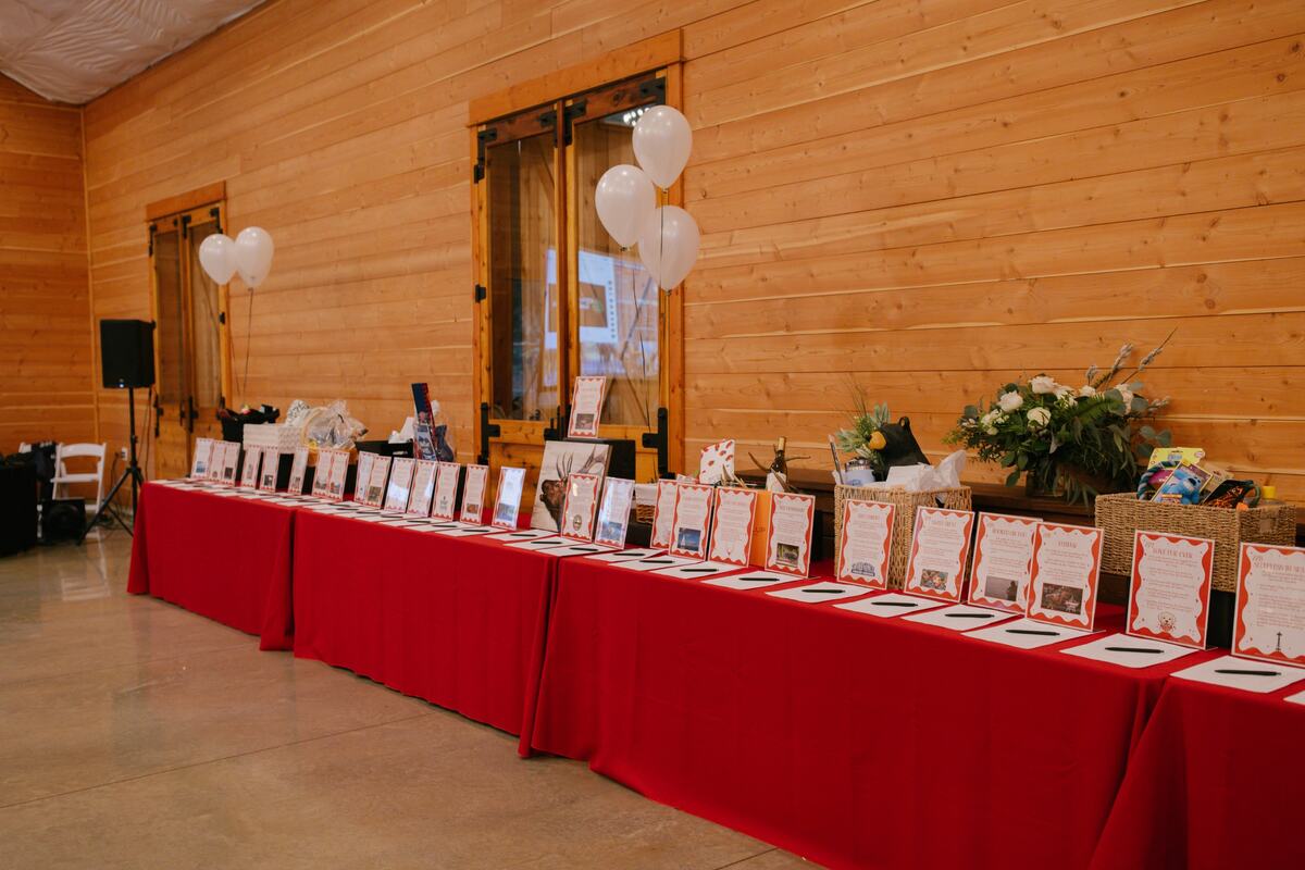 Silent auction tables with red linens and item cards along the cedar wall
