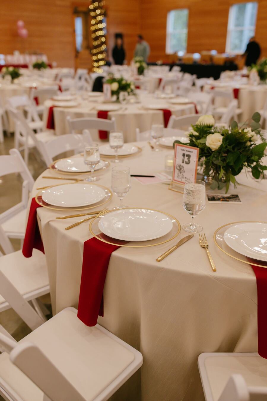 Round table set with gold-rimmed chargers, red napkins, and white floral centerpieces