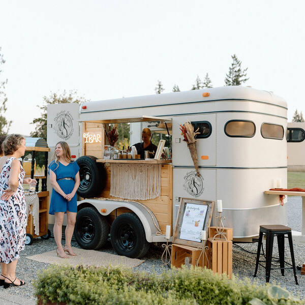 Guests at a vintage horse-trailer mobile bar on the gravel drive