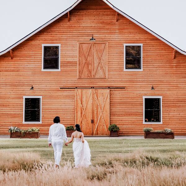 Couple walking through tall grass toward the barn