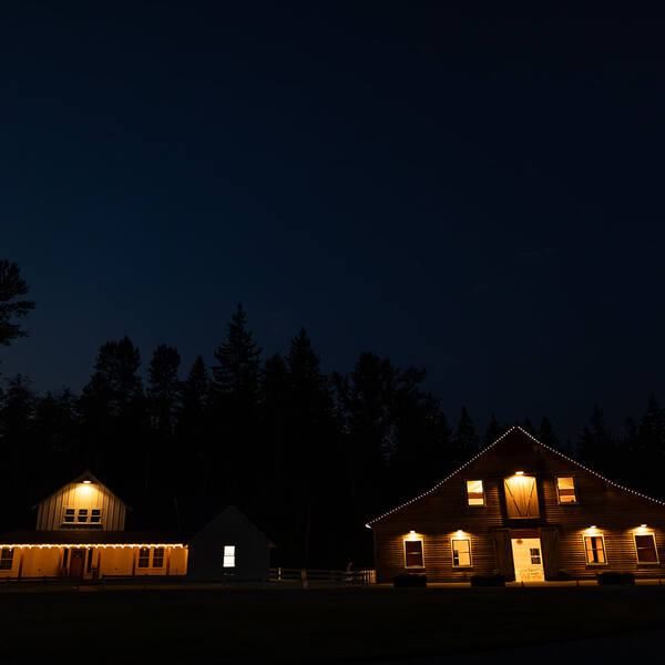 Cottage and barn lit up under a night sky