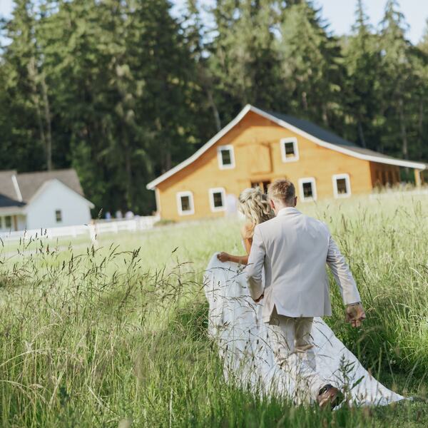 Couple wading through tall grass toward the barn and cottage