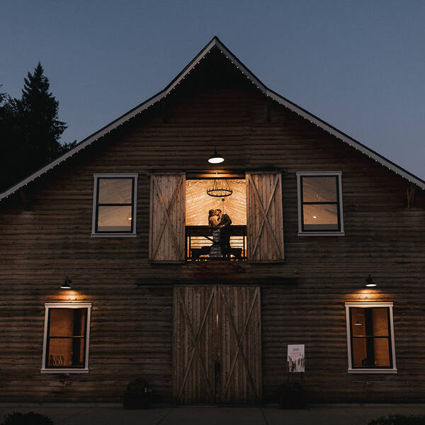 Couple kissing in the glowing loft door of the barn at blue hour