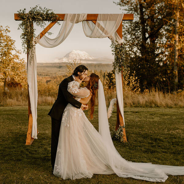 Kiss under the draped arbor with Rainier at golden hour