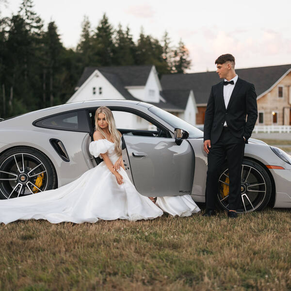 Couple by a sports car with the cottage and barn behind