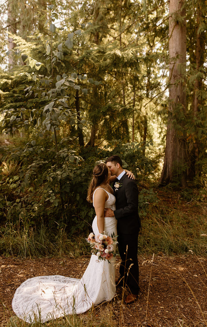 Couple kissing in the sunlit cedar grove, her lace train spread behind her