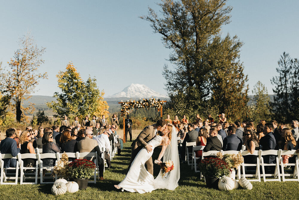 Couple kissing down the aisle in the meadow with golden fall trees and Mount Rainier
