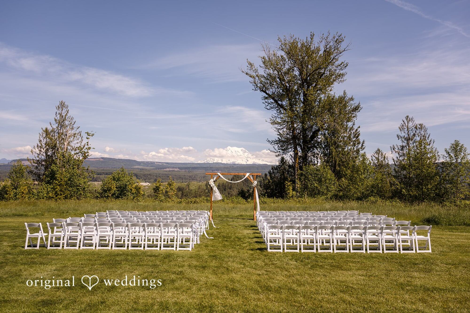 White ceremony chairs facing the wooden arbor in the meadow, with Mount Rainier behind