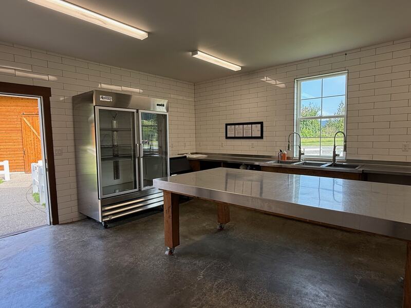 Catering kitchen with a stainless prep island, commercial glass-door cooler, and triple sink under a window