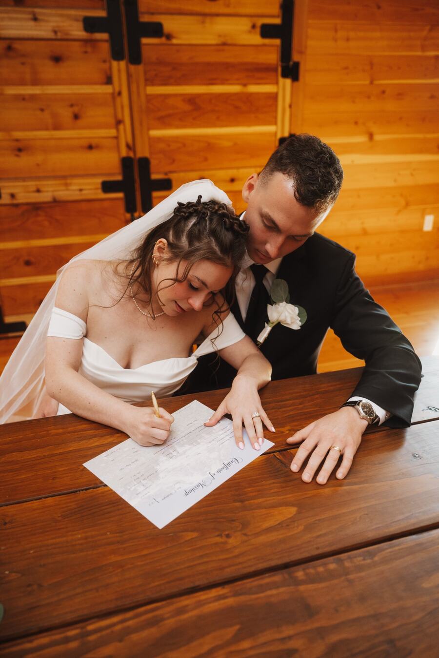 Newlyweds signing their marriage license at a wooden table in the loft