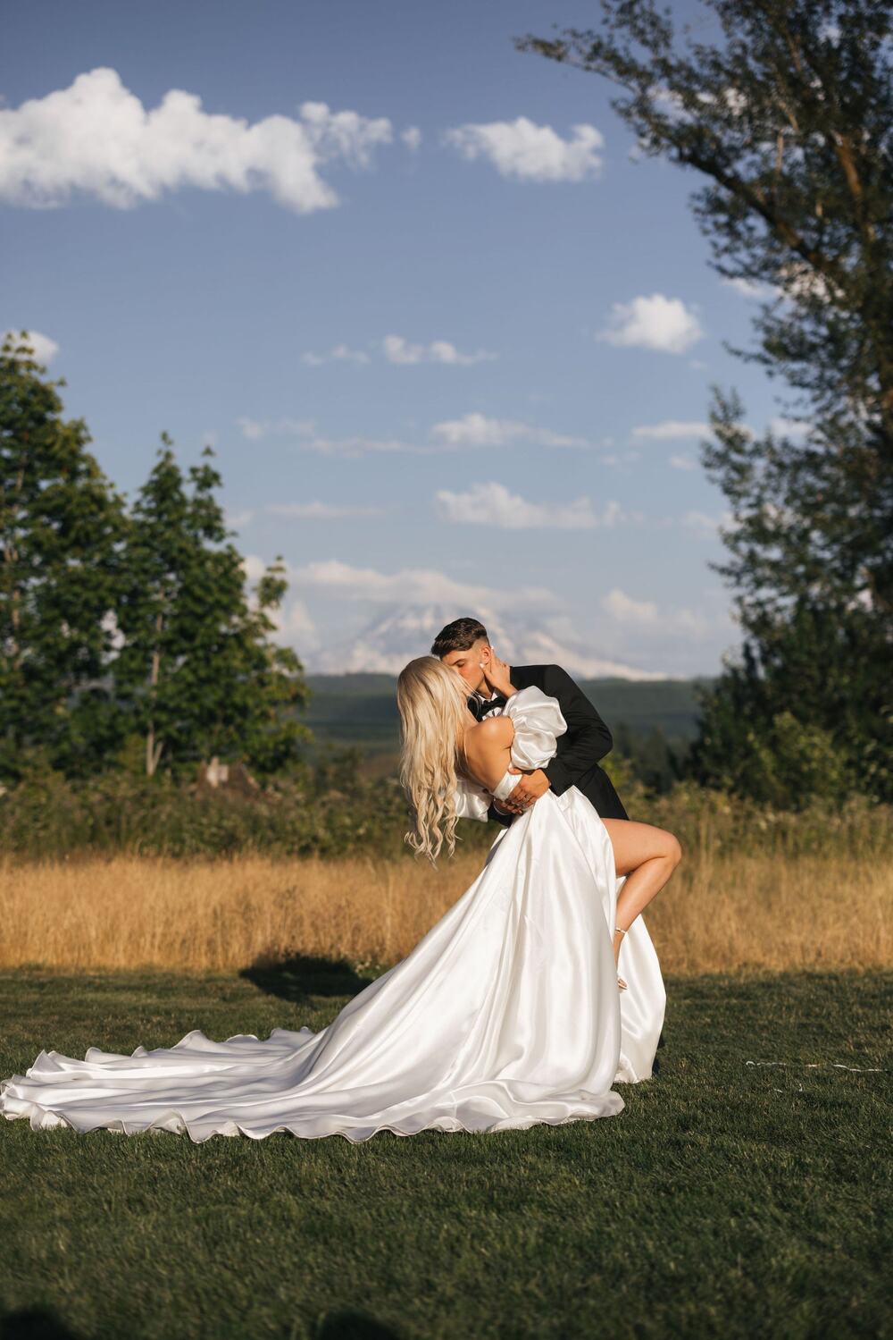 Groom dipping his bride in the meadow with Mount Rainier behind